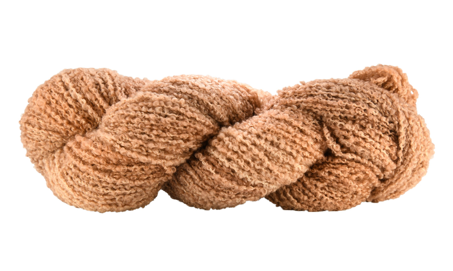 A twisted skein of Barn Yarn hand-dyed boucle DK weight yarn in colorway Pink Sand, a soft blush pink with sandy undertones, perfect for knitting and crochet projects.