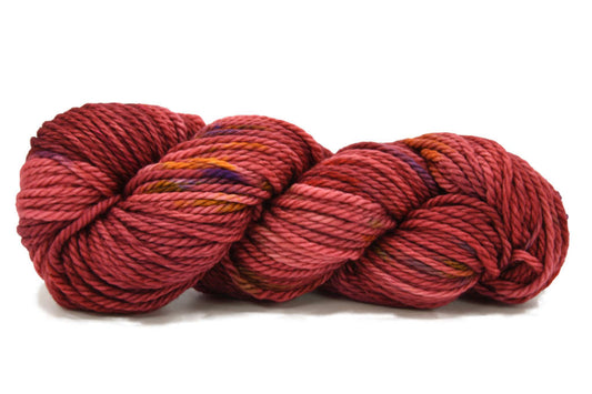 A twisted skein of Barn Yarn hand-dyed bulky weight yarn in colorway Smitten - reddish cinnamon with flecks of purple, orange, brown and red undertones, perfect for cozy knitting and crochet projects.