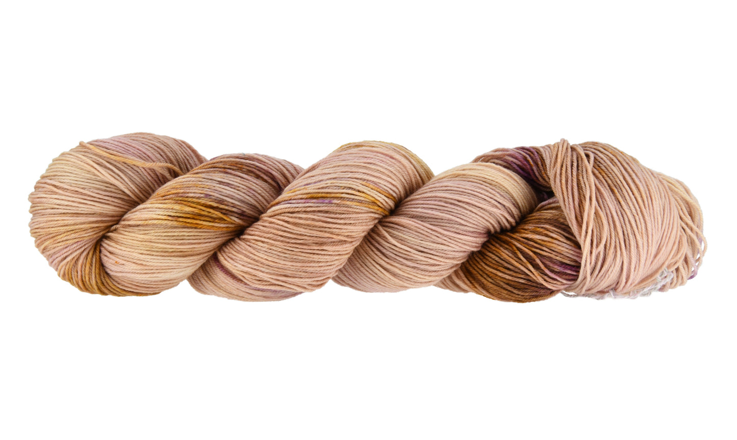 A twisted skein of Barn Yarn hand-dyed fingering weight yarn in colorway Nougat, a light pink, toffee, and purple combination, perfect for knitting and crochet projects.