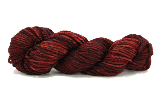 A twisted skein of Barn Yarn hand-dyed bulky weight yarn in Cinnabar - deep red with earthy undertones, perfect for bold and cozy knitting and crochet projects.
