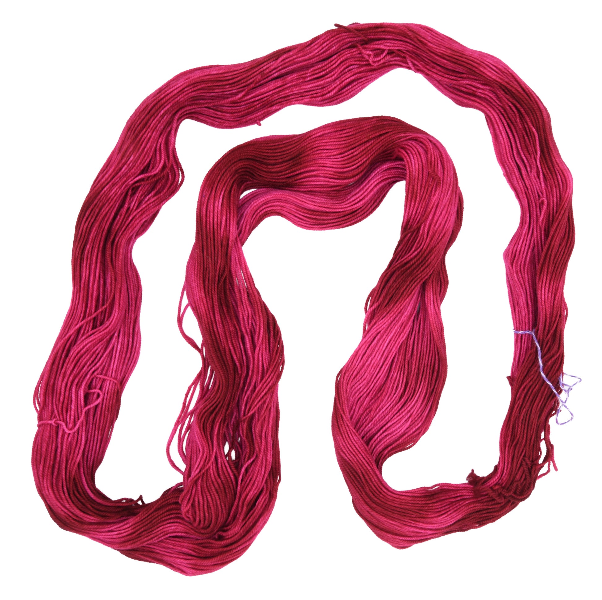 An unfolded hank of sport weight hand-dyed yarn in colorway Pomegranate featuring layered bright and dark saturated pink tones, ideal for vibrant handmade creations.