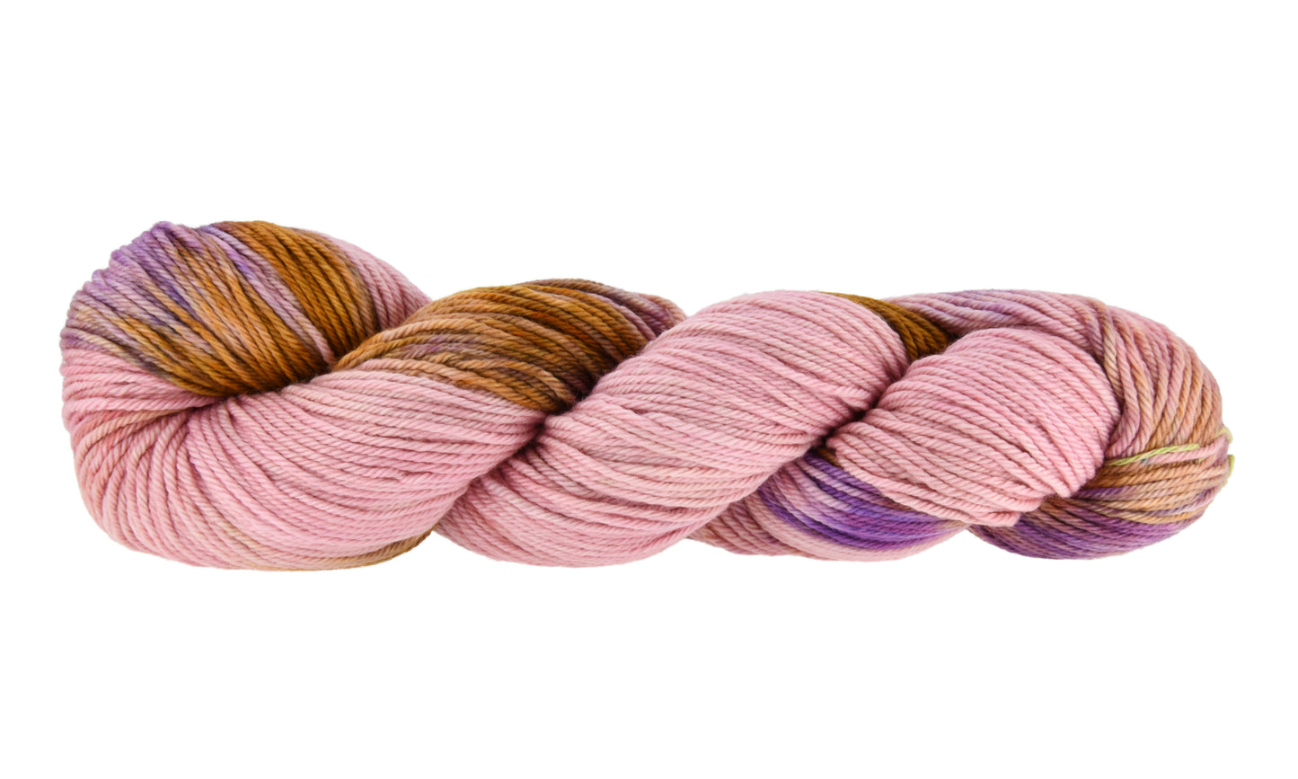 A twisted skein of Barn Yarn hand-dyed worsted weight yarn in colorway Nougat, a light pink, toffee, and purple combination, perfect for knitting and crochet projects.