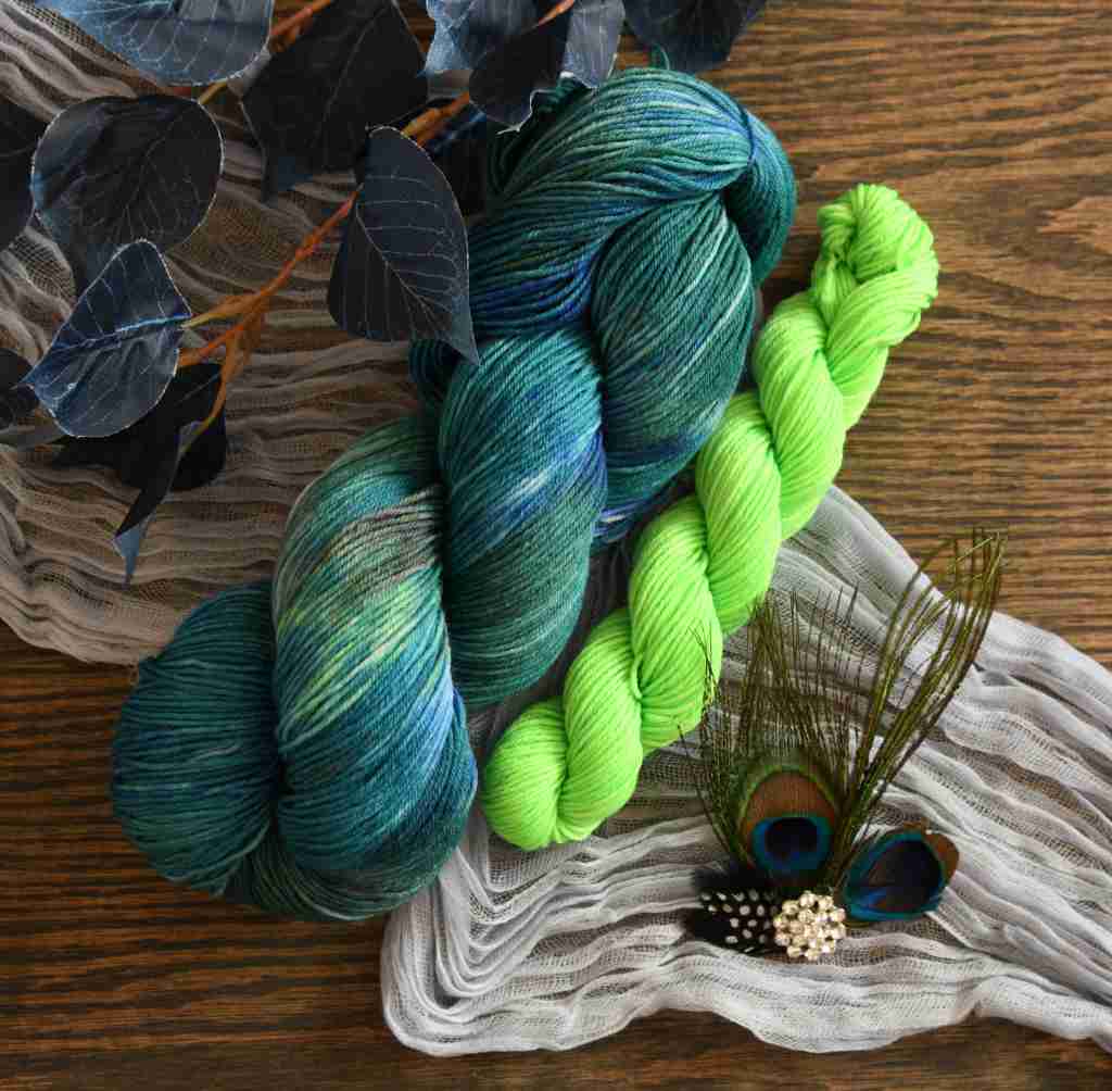Twisted skeins of Barn Yarn hand-dyed green mini and coordinating yarn in colorway Play the Peacock-vibrant teal, emerald green, rich blue inspired by the colors of a peacock’s feathers.