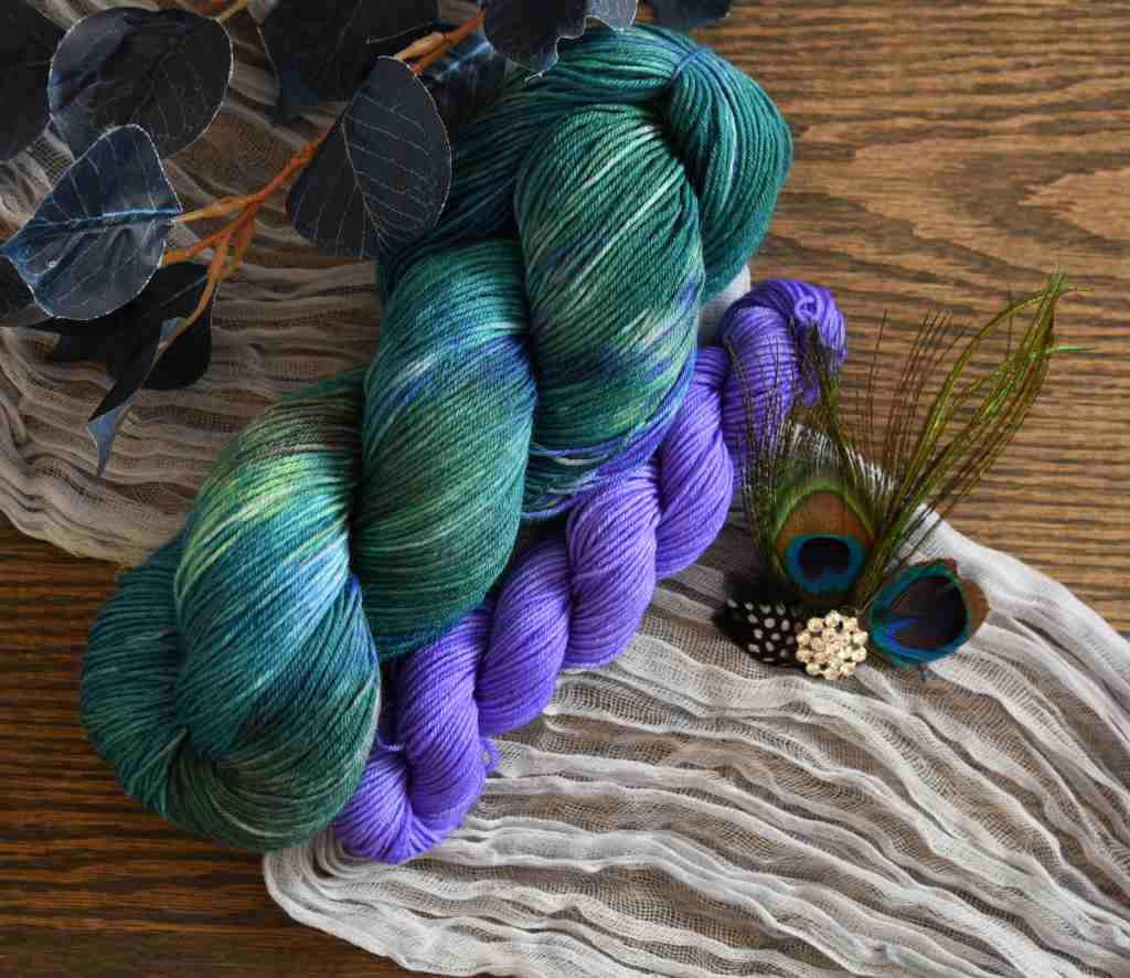Twisted skeins of Barn Yarn hand-dyed purple mini and coordinating yarn in colorway Play the Peacock-vibrant teal, emerald green, rich blue inspired by the colors of a peacock’s feathers.