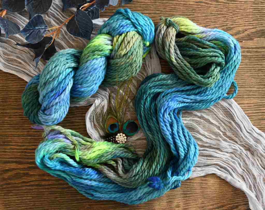 A twisted skein and an unfolded skein of Barn Yarn hand-dyed super-bulky weight yarn in colorway Play the Peacock -vibrant teal, emerald green, rich blue inspired by the colors of a peacock’s feathers.