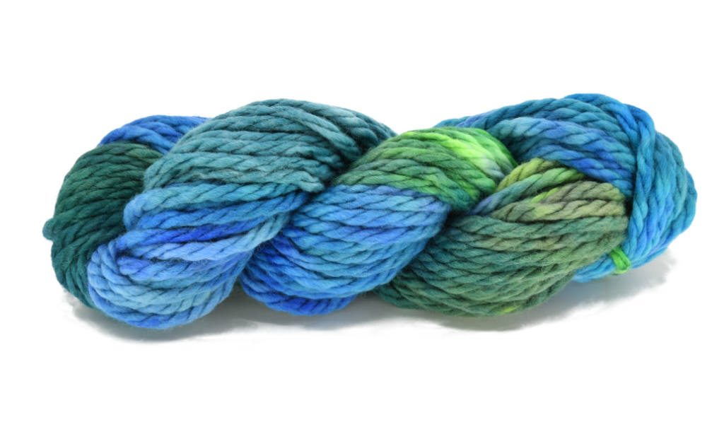 A twisted skein of Barn Yarn hand-dyed super-bulky weight yarn in colorway Play the Peacock -vibrant teal, emerald green, rich blue inspired by the colors of a peacock’s feathers.