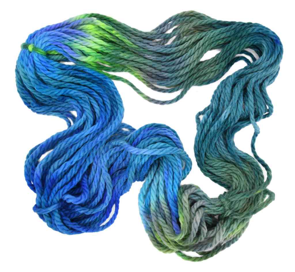 An unfolded skein of Barn Yarn hand-dyed super-bulky weight yarn in colorway Play the Peacock -vibrant teal, emerald green, rich blue inspired by the colors of a peacock’s feathers.