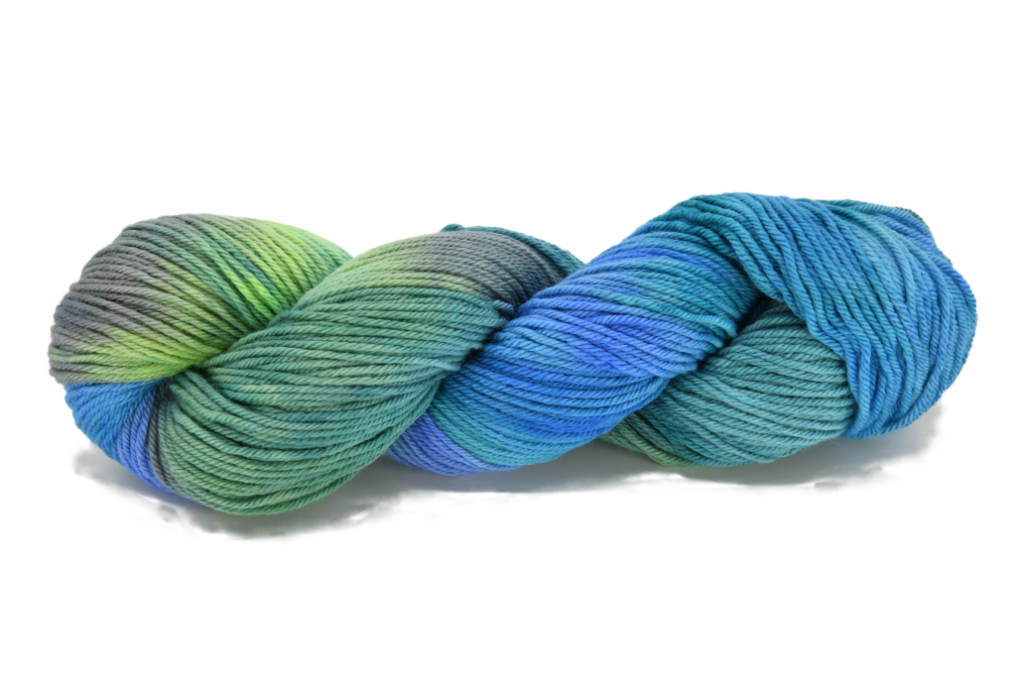 A twisted skein of Barn Yarn hand-dyed worsted weight yarn in colorway Play the Peacock -vibrant teal, emerald green, rich blue inspired by the colors of a peacock’s feathers.
