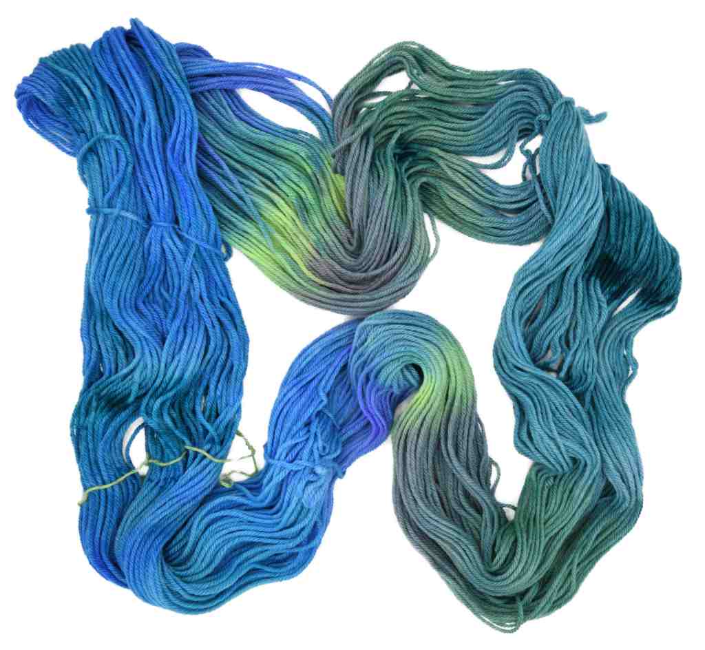 An unfolded skein of Barn Yarn hand-dyed worsted weight yarn in colorway Play the Peacock -vibrant teal, emerald green, rich blue inspired by the colors of a peacock’s feathers.